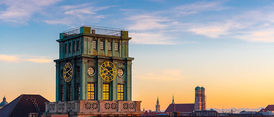 In the foreground the historic clock tower of the TUM, in the background the Frauenkirche - in evening mood
